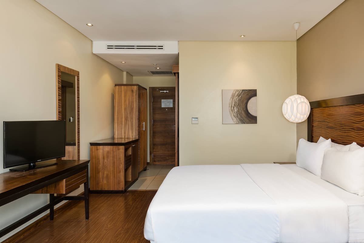 A hotel room with a large bed, a TV on a wooden stand, a wardrobe, and a mirror.