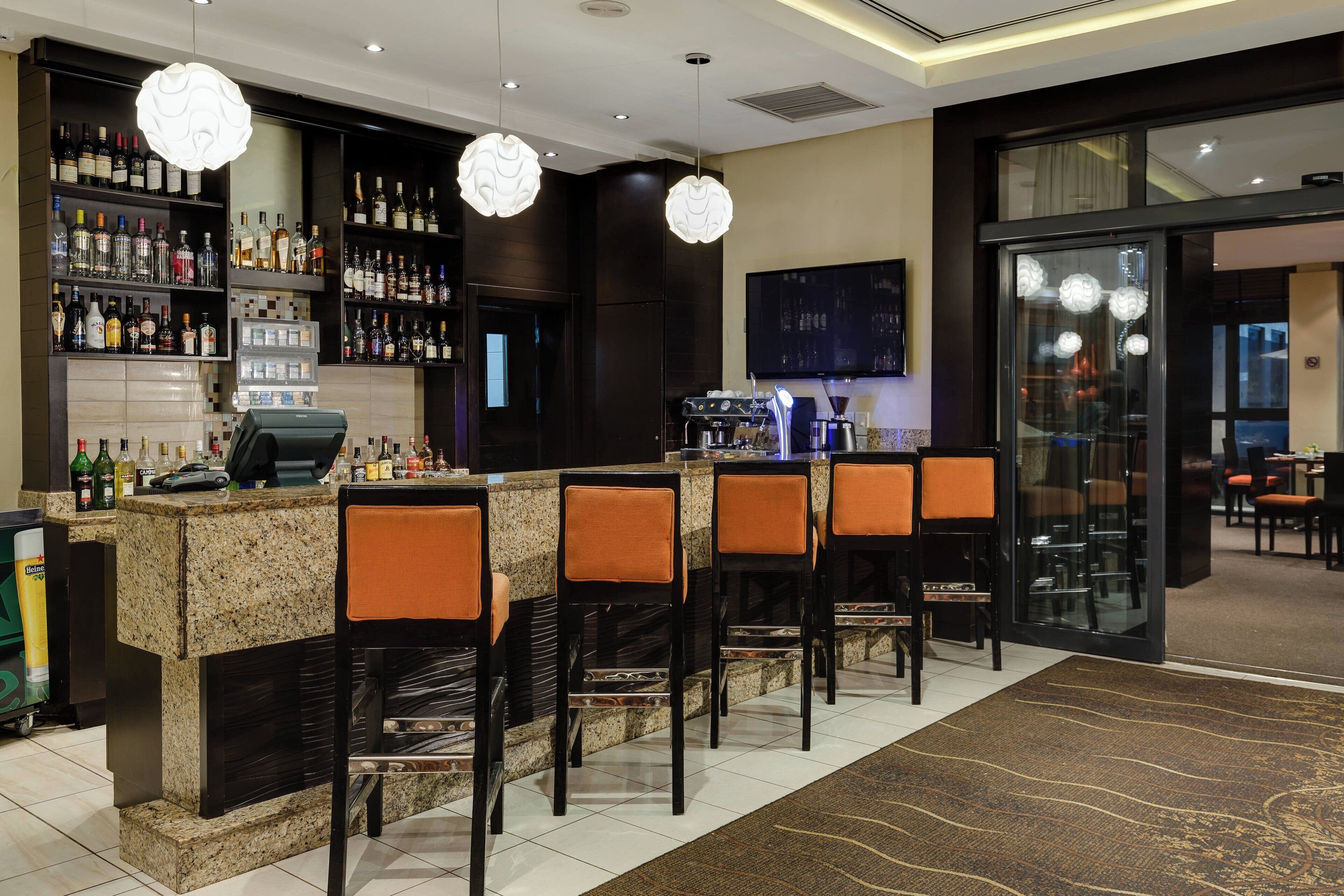 A bar area with a granite counter, multiple bar stools, and a variety of liquor bottles.