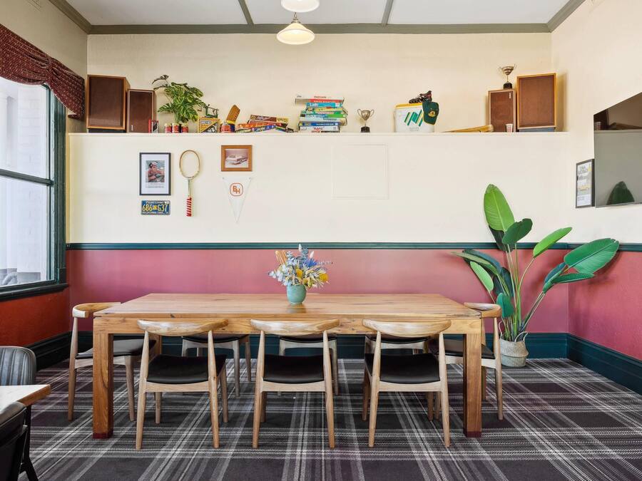 A dining area with a wooden table and chairs, a plaid carpet, and a wall decorated with books, trophies, and framed pictures.