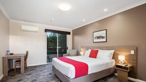 A hotel room with a bed, a desk, a chair, a nightstand, and a window with a view of greenery. - Quality Hotel Bayswater (Bayswater)