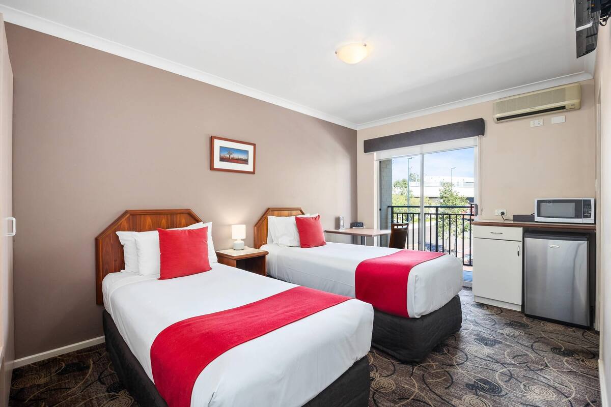 A hotel room with two beds, a kitchenette, a small dining area, and a balcony with a view.
