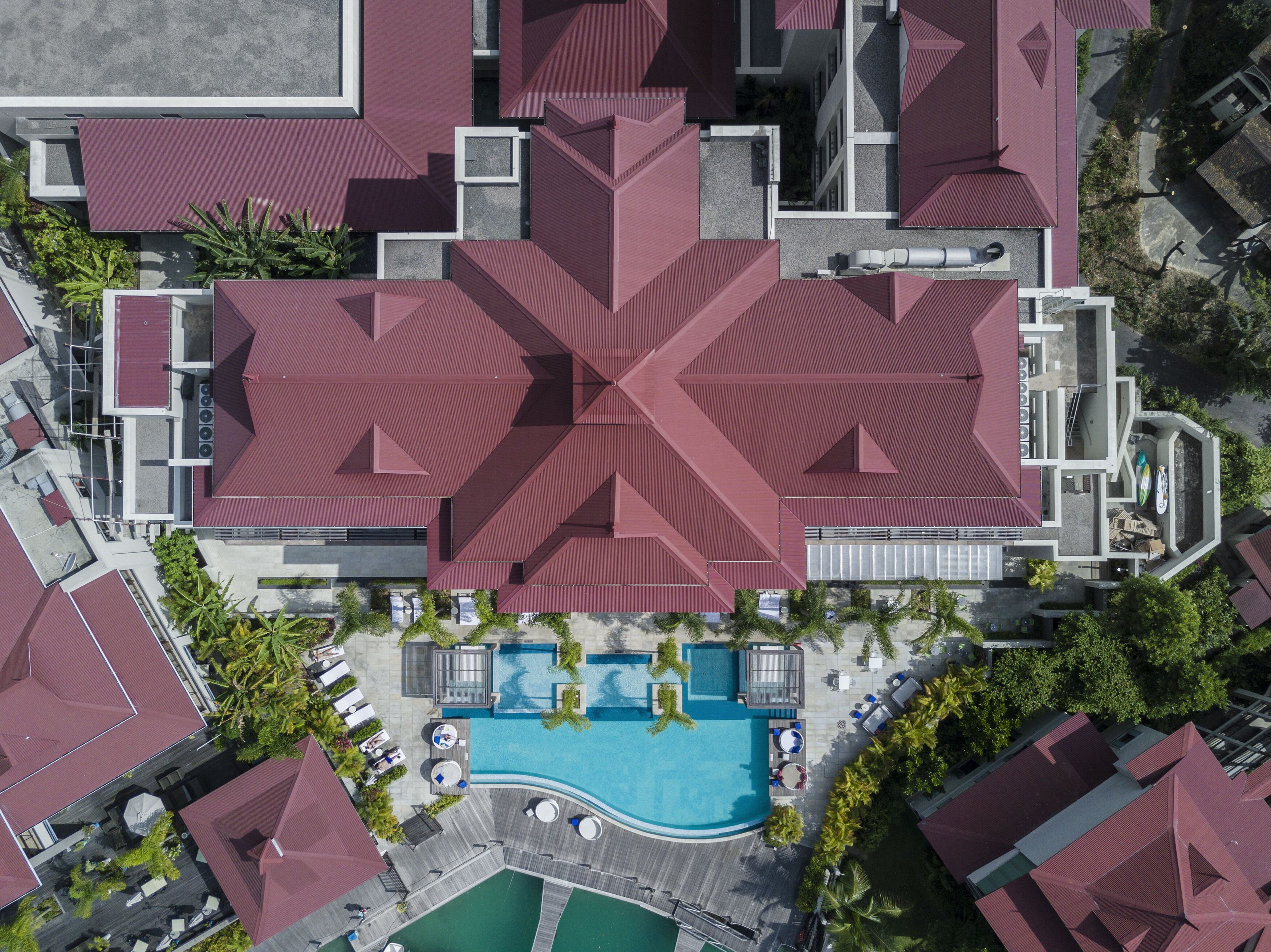 Eine Vogelperspektive zeigt ein Hotel mit einem markanten roten Dach, einem Swimmingpool und Außenbereichs-Sitzgelegenheiten.