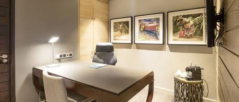 A modern conference room with a large table, two chairs, a round side table with a coffee machine, and three framed artworks on the wall.