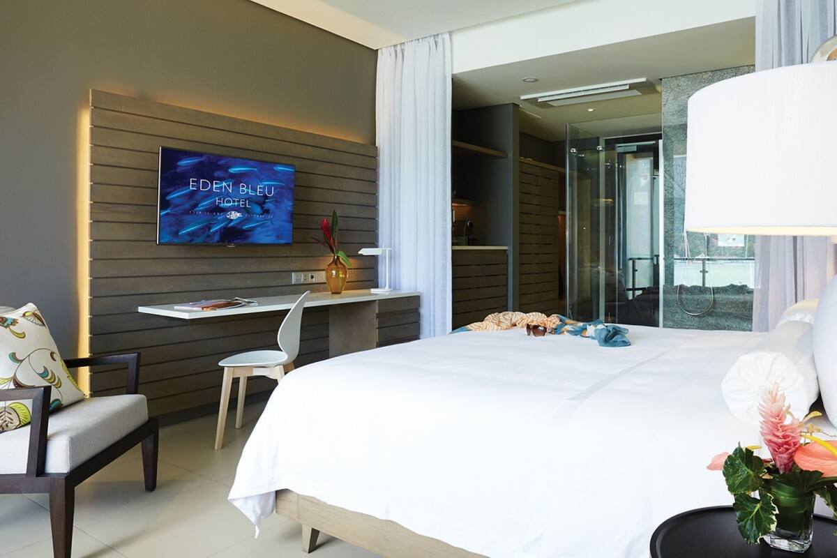 A modern hotel room with a large bed, a desk, a TV, and a view through a glass door.