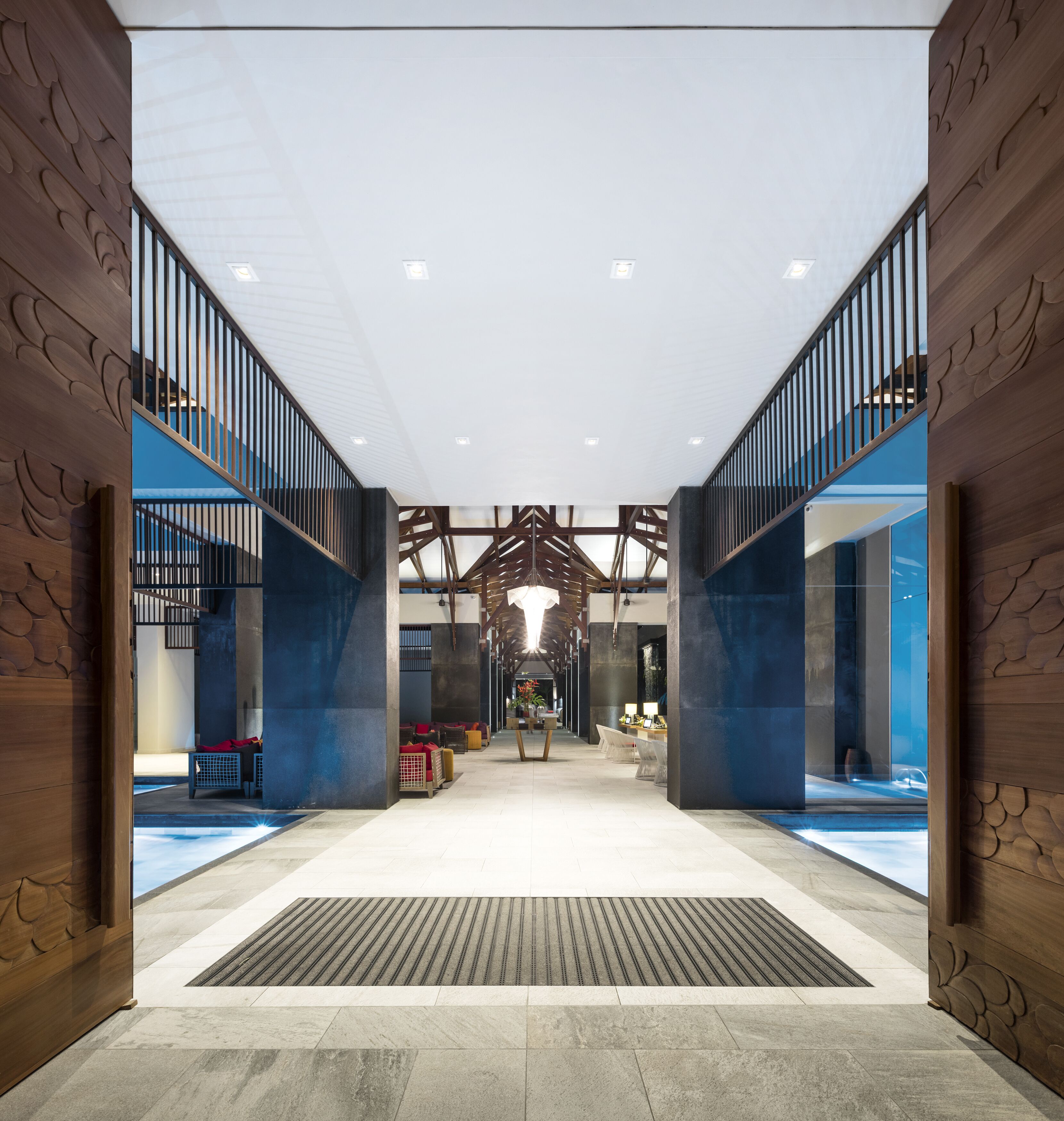 Eine großzügige Lobby mit hoher Decke, Holzvertäfelungen an den Wänden und einer zentralen Sitzecke mit Sofas und Tischen.
