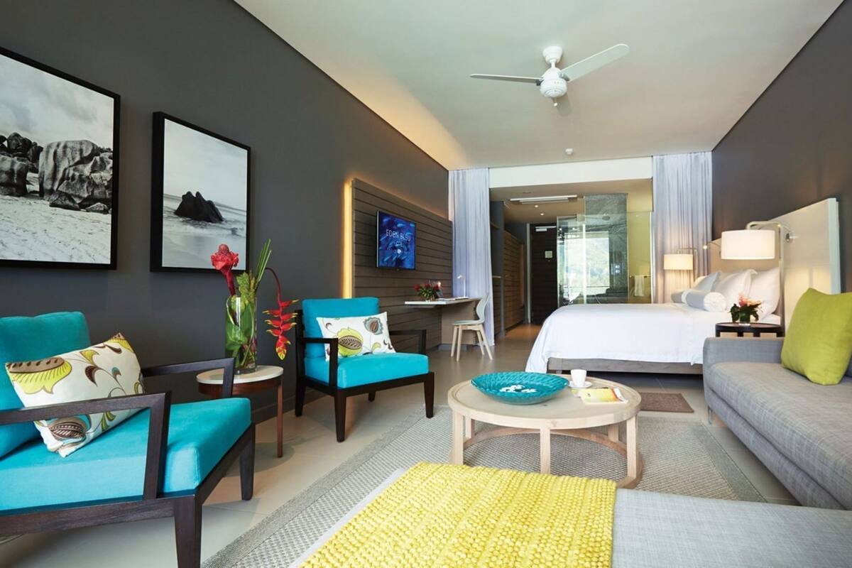 A hotel room with a bed, a sofa, a chair, a small table, and a TV.
