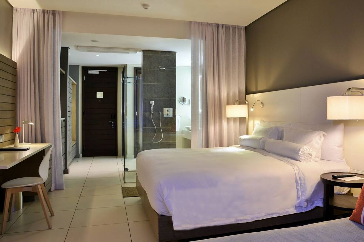 A hotel room with a bed, bedside table, lamp, and a desk with a chair.