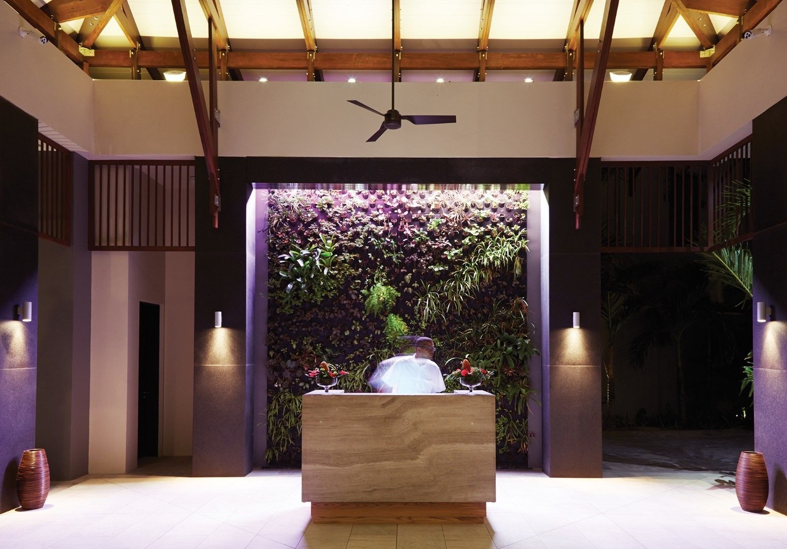 Una moderna zona de recepción con un mostrador de madera, un ventilador de techo y una pared decorada con plantas.