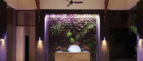 Una moderna zona de recepción con un mostrador de madera, un ventilador de techo y una pared decorada con plantas.