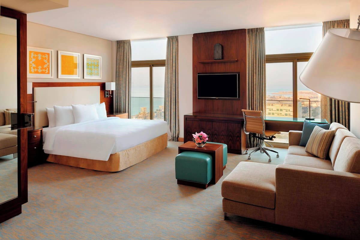 A hotel room with a large bed, a sofa, a TV, and a view of the city.