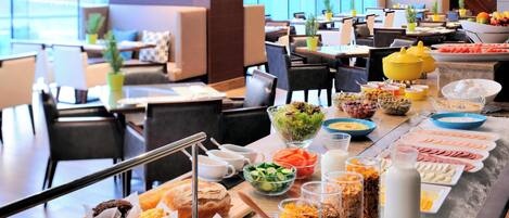 Un bufé con diversas opciones de comida y bebidas, como pasteles, ensaladas y fruta.