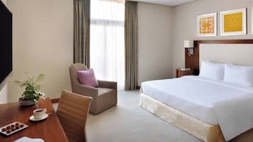 A hotel room with a bed, a chair, a table with a plant and a cup, and a window with curtains.