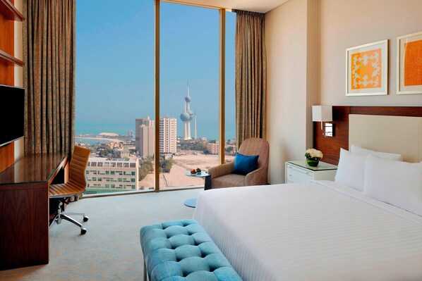 A hotel room with a large bed, a desk, a chair, and a view of a cityscape with a tower. - Residence Inn by Marriott Kuwait City (Kuwait City)