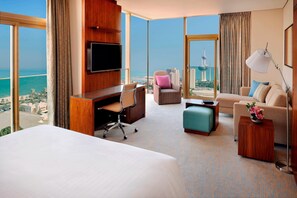 A hotel room with a large bed, a desk with a chair, a sofa, a small table, and a TV. There is a view of the city and a tower in the background. - Residence Inn by Marriott Kuwait City (Kuwait City)