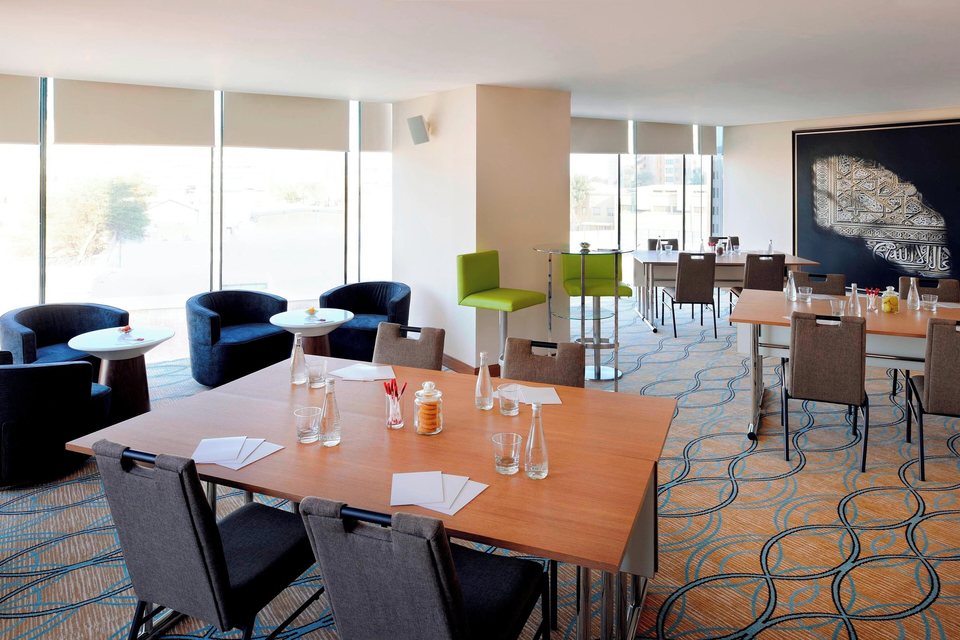 Une salle de conférence d’hôtel avec une grande table, de nombreuses chaises et une vue dégagée grâce à de grandes fenêtres.