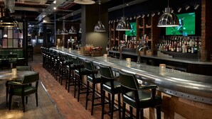 A bar area with a long counter, multiple bar stools, and a variety of bottles and glasses. - Village Hotel Aberdeen (Aberdeen)