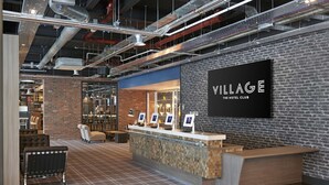 A reception area with a check-in counter, seating, and a brick wall with a sign reading "ILLAGE THE HOTEL CLUB". - Village Hotel Aberdeen (Aberdeen)