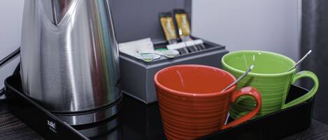 Una bandeja negra con una cafetera de acero inoxidable, una taza roja y una taza verde.