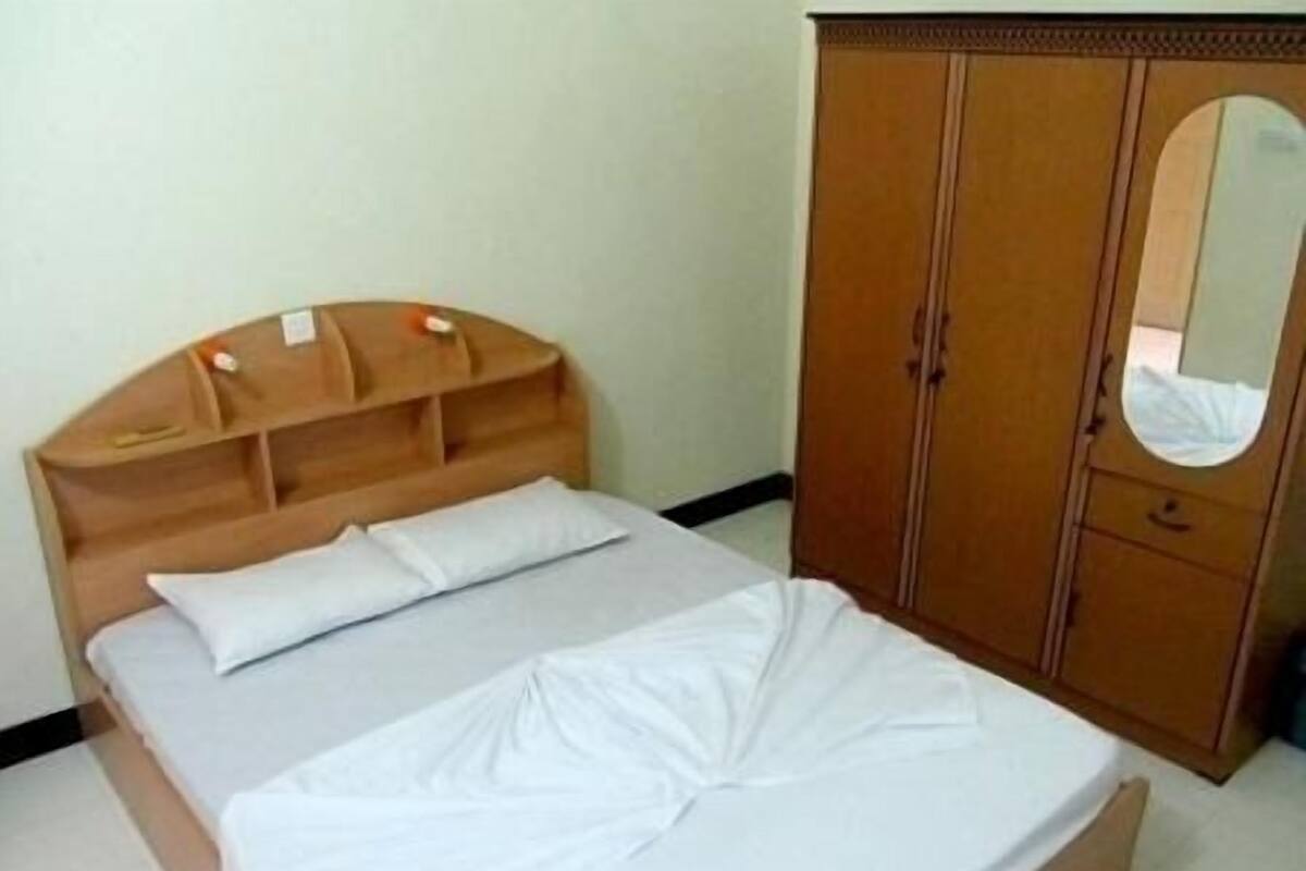 A bedroom with a wooden headboard, a single bed with white bedding, and a wooden wardrobe with a mirror.