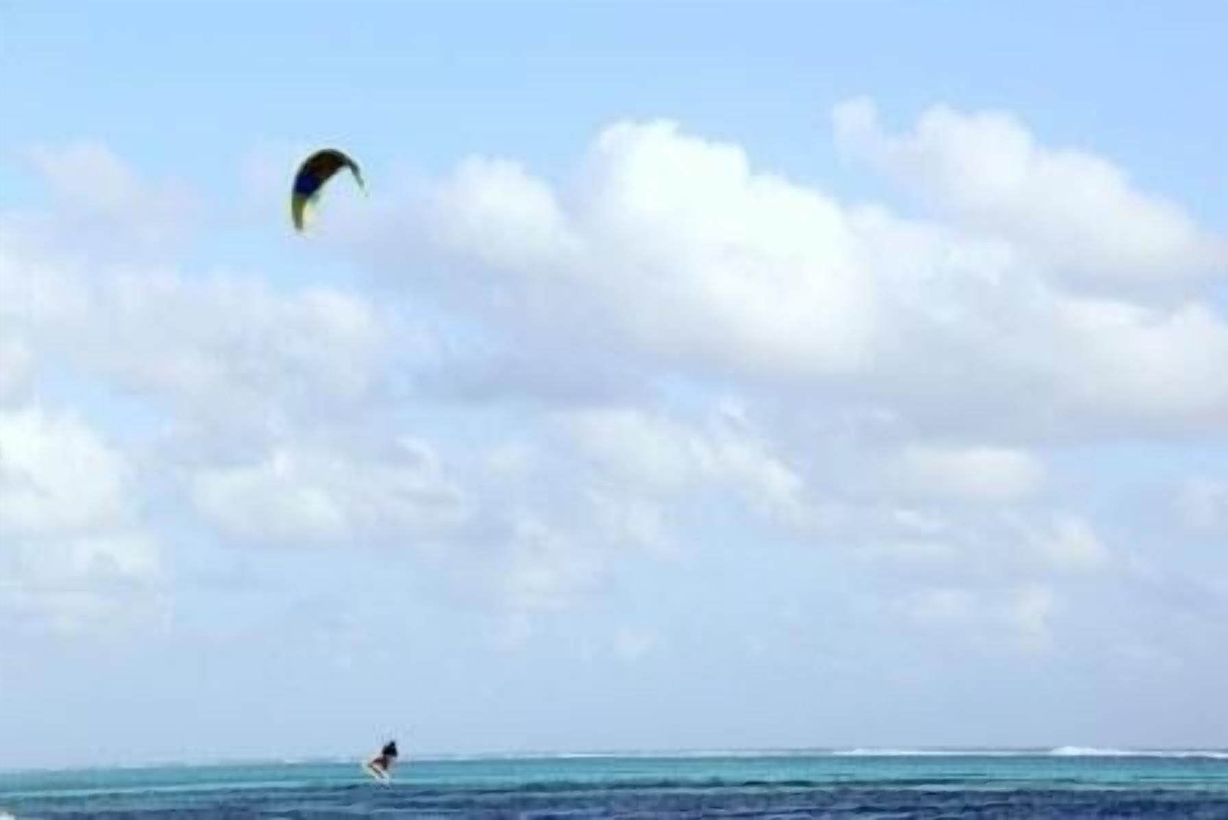 A person kite surfing in the ocean with a clear sky and clouds.