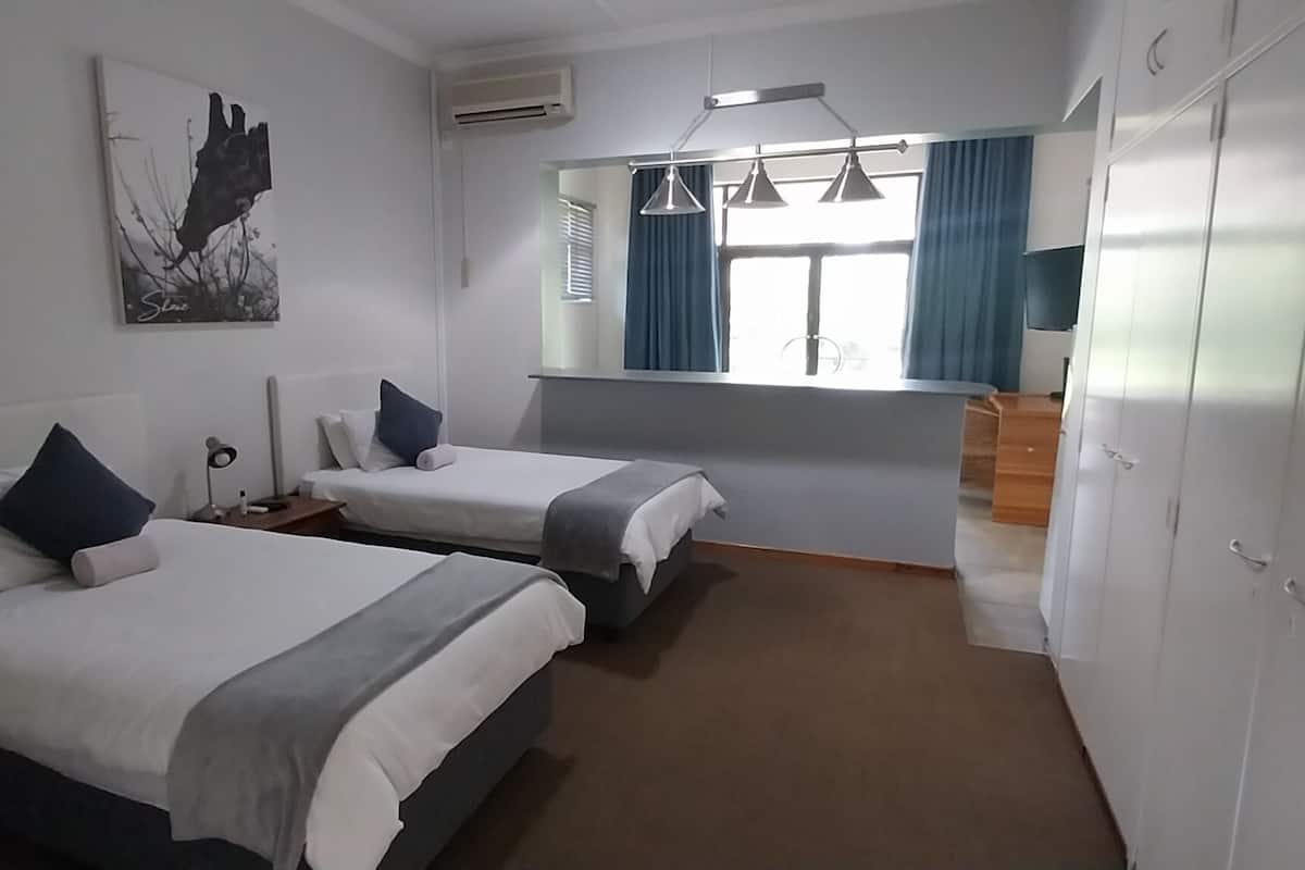 A hotel room with two beds, a large window with curtains, a painting on the wall, and a wardrobe.