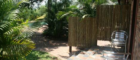 Un espace patio doté d’un sol carrelé, d’une clôture en bambou et d’une chaise en métal.