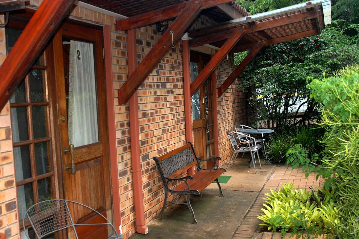 A brick building with a wooden porch, a bench, and a table with chairs.