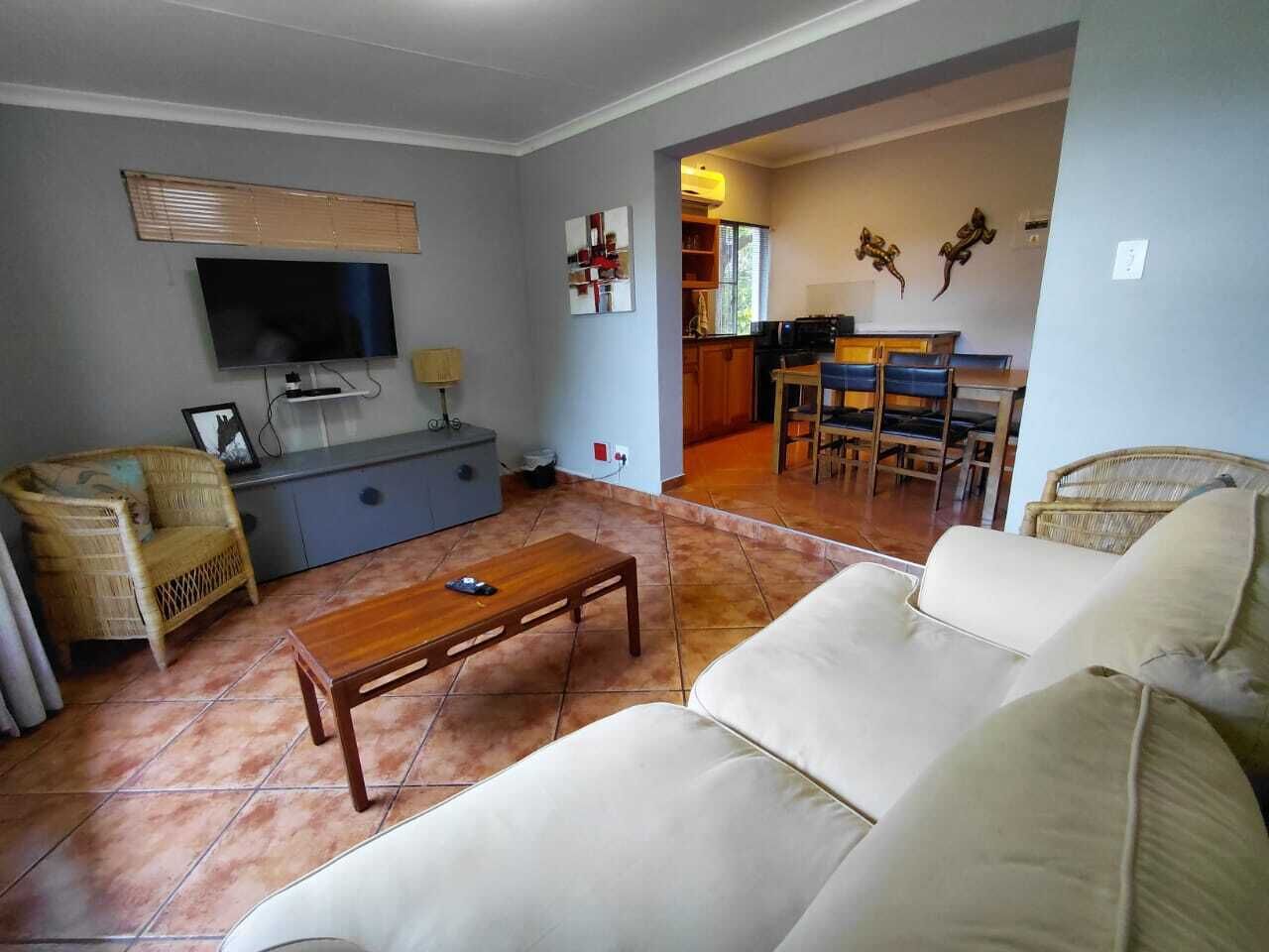 A living room with a sofa, a wooden coffee table, a television, a wicker chair, and a kitchen area in the background.