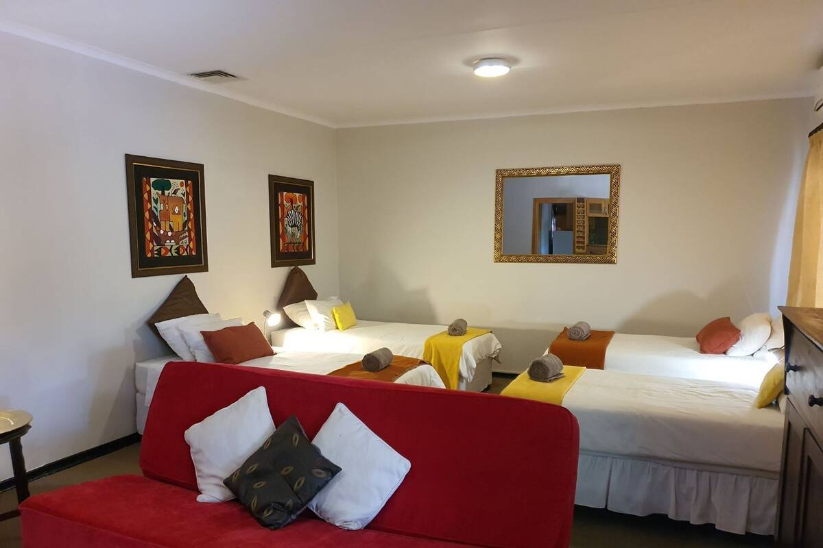 A hotel room with two single beds, a red sofa, and two paintings on the walls.