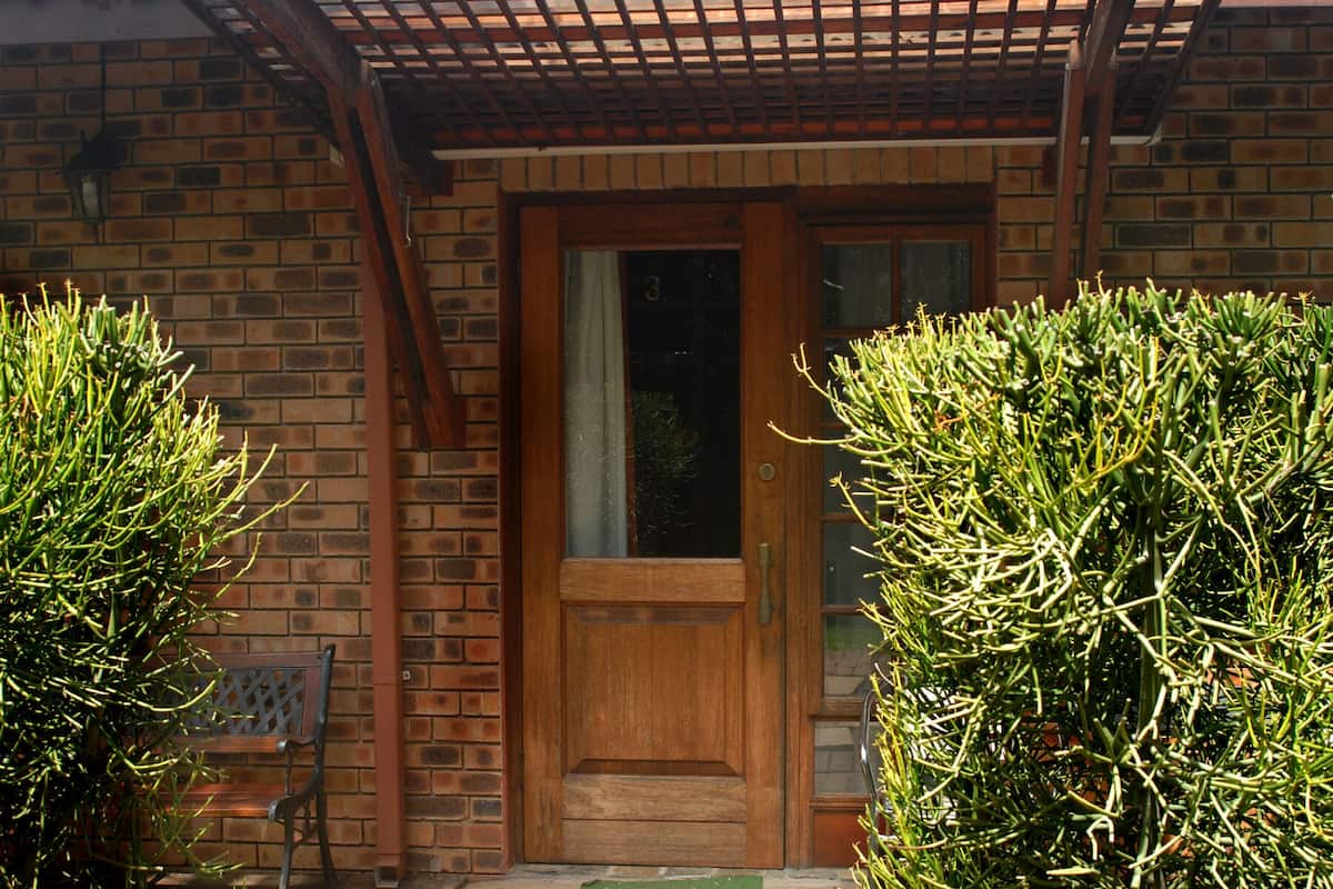 A wooden door with a glass panel, a brick wall, and a wooden pergola.