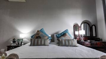 Una habitación de hotel con una cama grande, dos almohadas, una mesita de noche con lámpara, un espejo y un aparador.