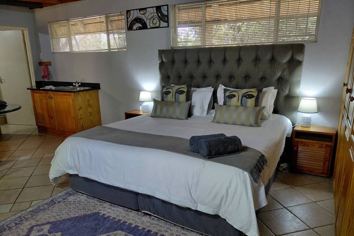 A bedroom with a large bed, two bedside tables, a nightstand, a wooden cabinet, and a patterned rug.