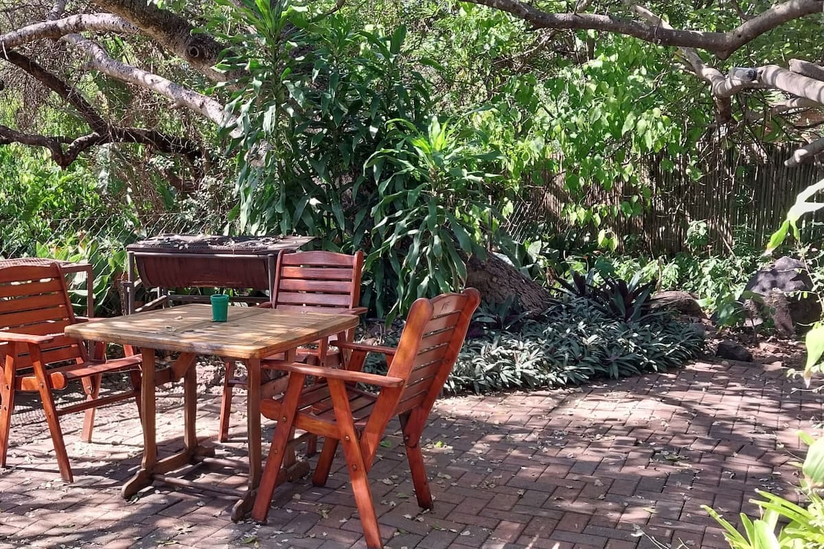 An outdoor seating area with a table and chairs, surrounded by lush greenery and trees.