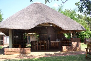 Una estructura al aire libre con techo de paja, base de ladrillo, muebles de madera y chimenea de ladrillo.
