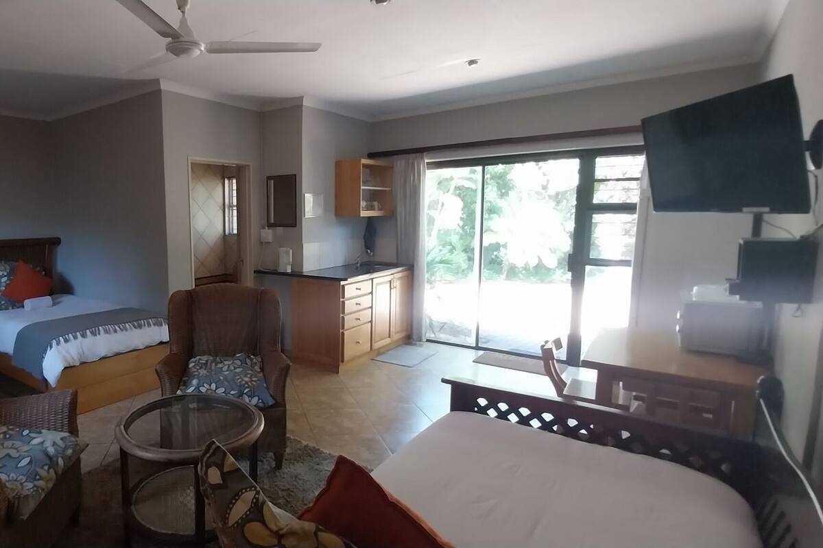 A spacious room with a bed, two chairs, a small table, a TV, and a kitchen area.