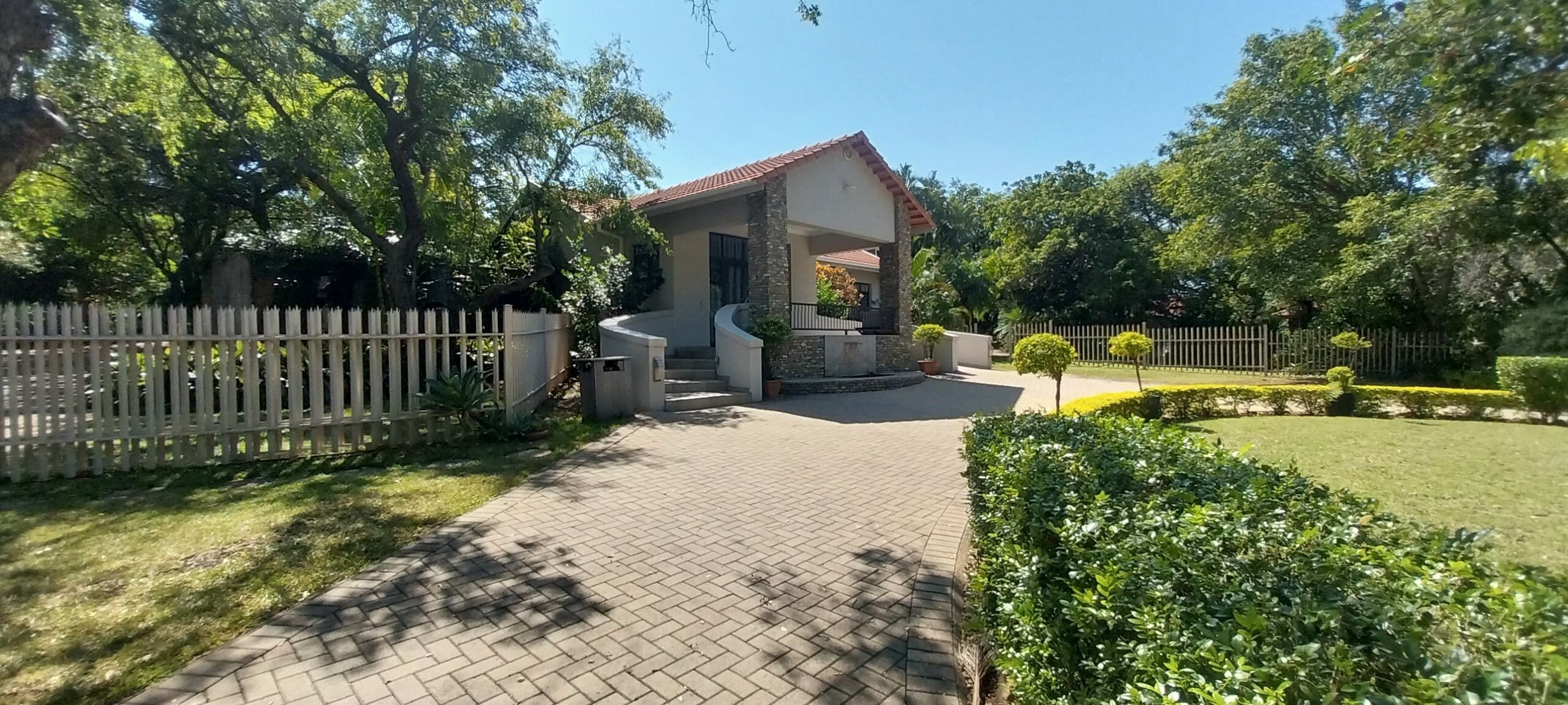 Una casa amb un carrer d'accés pavimentat, una tanca blanca de palets i un jardí ben cuidat.