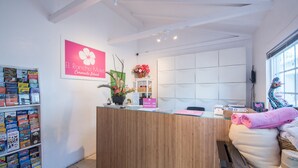 A reception desk with a wooden counter, a sign for El Rancho Motel, a flower arrangement, and a window with blinds. - El Rancho Motel (Coronado)