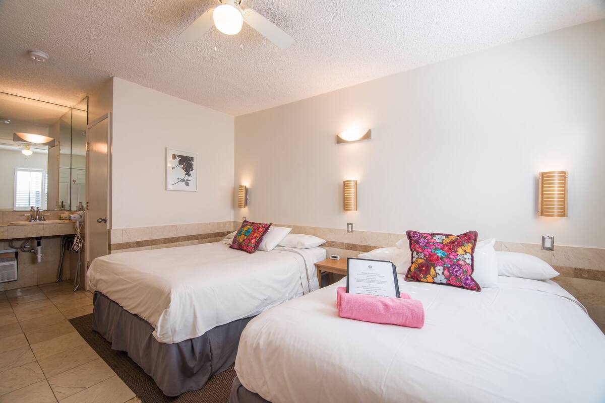 Una habitación de hotel con dos camas, un baño y un espejo.
