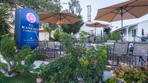 A patio area with outdoor seating, a sign for El Rancho Coronado, and surrounding greenery. - El Rancho Motel (Coronado)