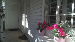 A porch with a tiled floor and a door leading inside. There are two potted plants with pink flowers on the right side. - El Rancho Motel (Coronado)