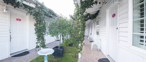 Un espacio al aire libre cubierto con un pequeño jardín, una puerta blanca y una silla blanca.