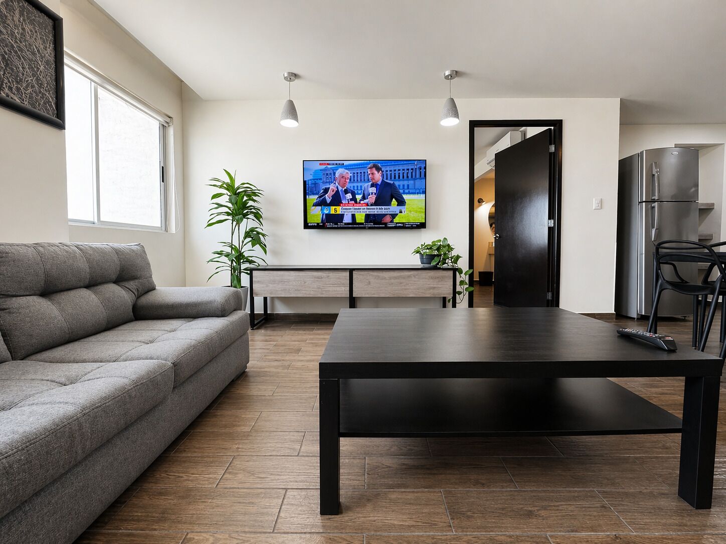 A modern living room with a sofa, a coffee table, a TV, and a kitchen area with a refrigerator.