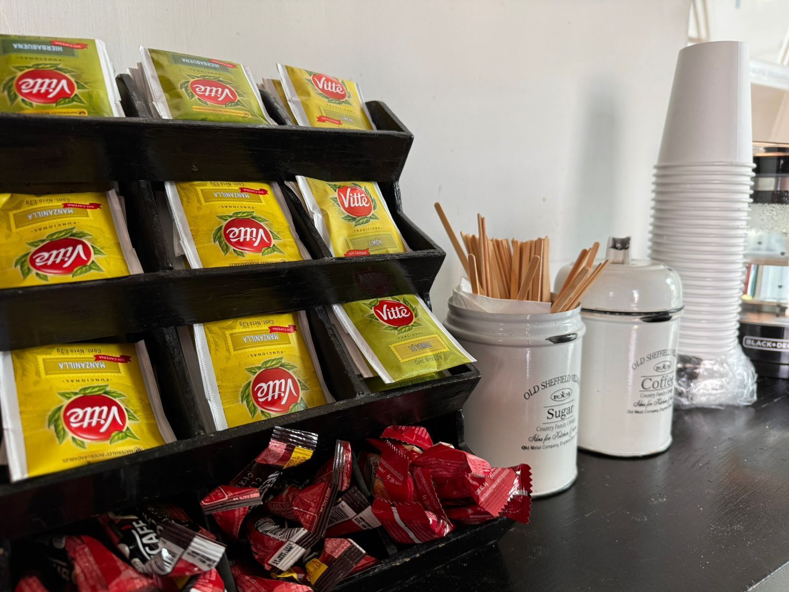 A beverage station with multiple packs of Vittel water, a jar of sugar, and a container of coffee.