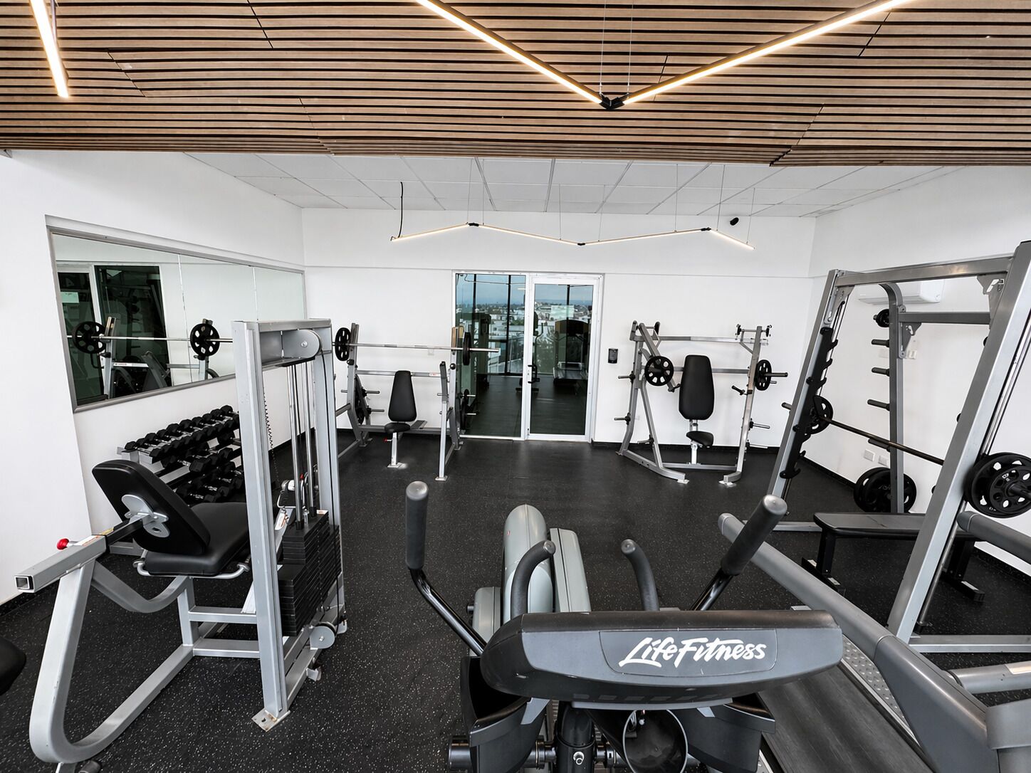 Un gimnasio con equipo de levantamiento de pesas, cintas de correr y un espejo grande.