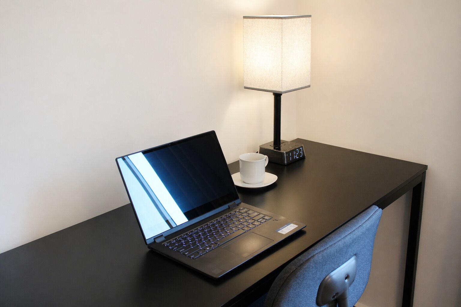 A laptop on a desk with a lamp and a cup.