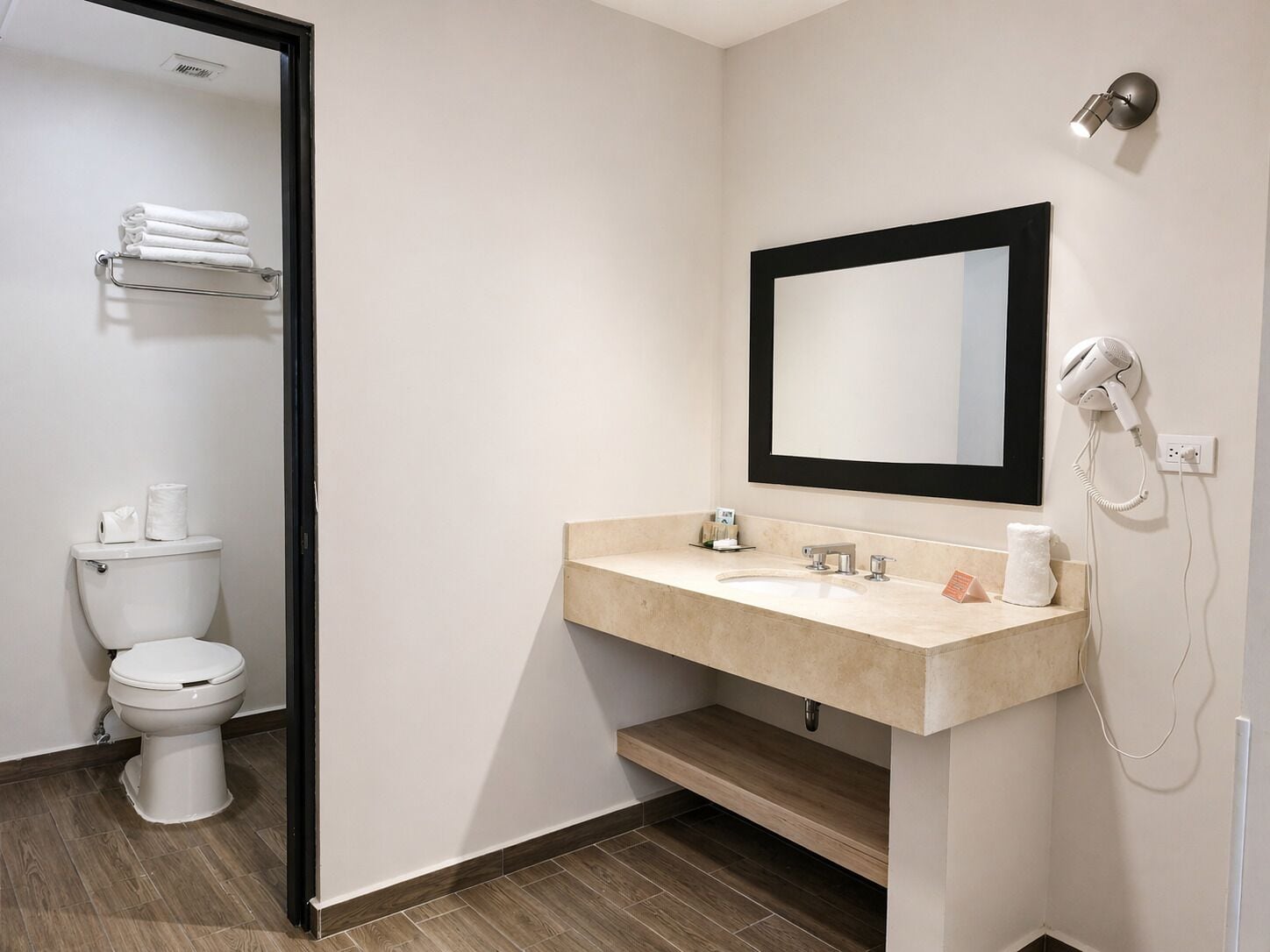 A modern bathroom with a toilet, sink, mirror, and hairdryer.