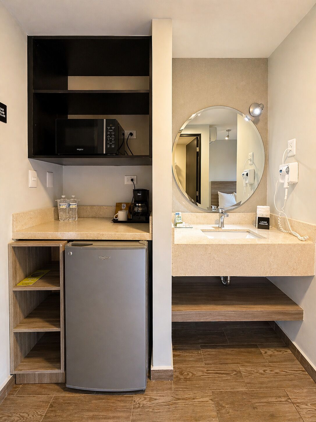 A compact kitchenette with a built-in microwave, a small refrigerator, a coffee maker, and a sink with a mirror above it.