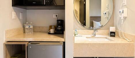 A compact kitchenette with a built-in microwave, a small refrigerator, a coffee maker, and a sink with a mirror above it.