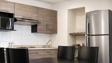 A modern kitchen with wooden cabinets, a stainless steel refrigerator, a microwave, and a dining area with chairs.