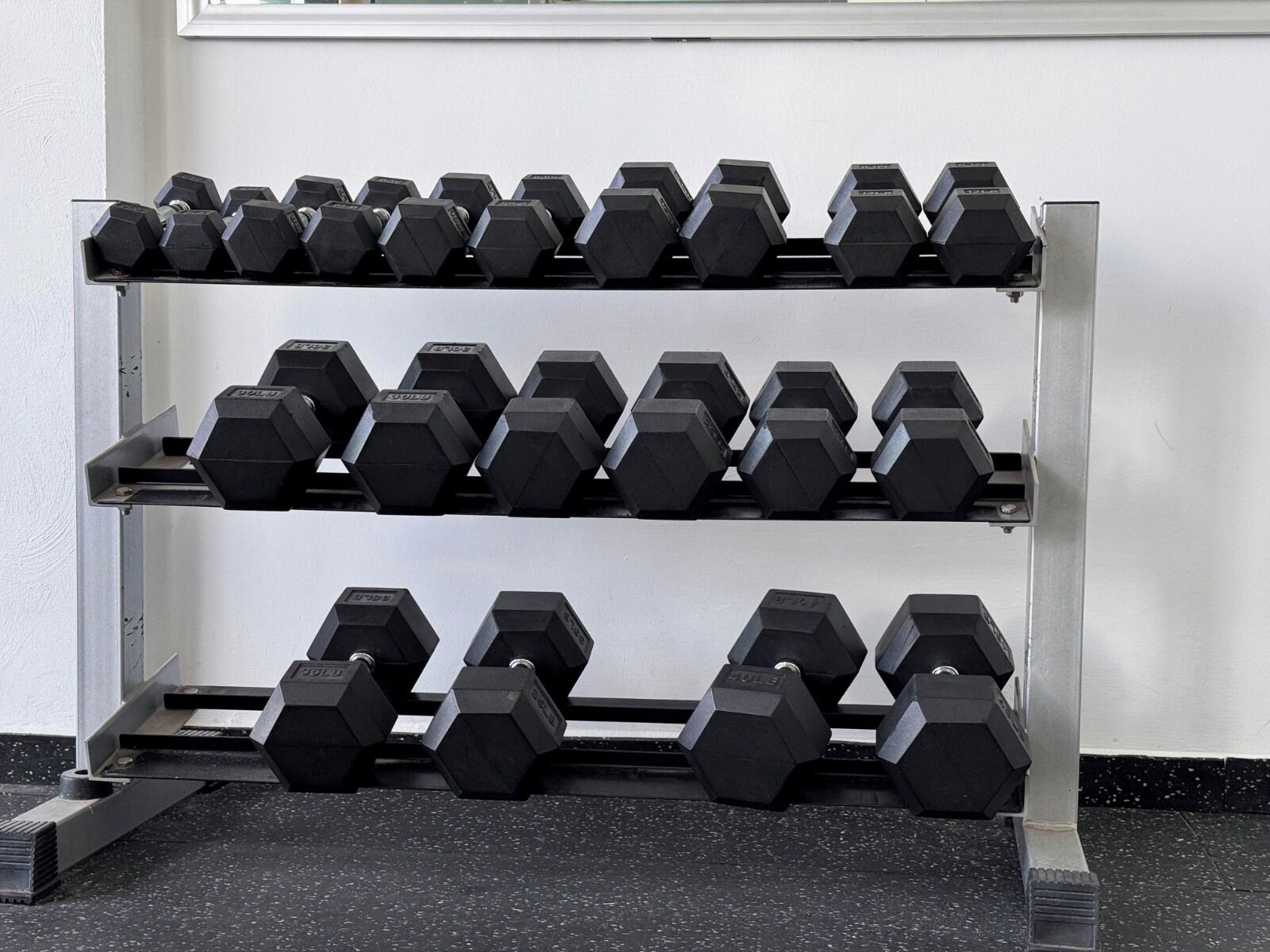 A rack of hexagonal dumbbells arranged in three rows against a white wall.
